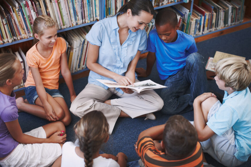 A pretty teacher sitting with her excited students in the library