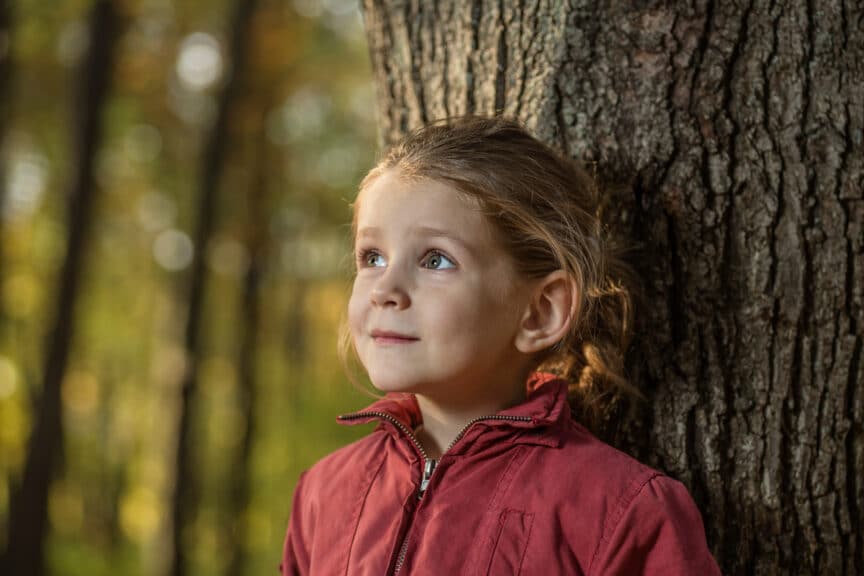 A young girl leaning against a tree trunk