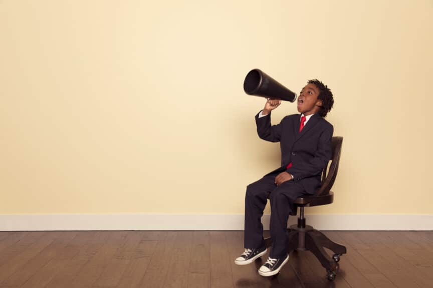 Boy-in-Business-Suit-Sitting-on-Chair-Yells-through-Megaphone