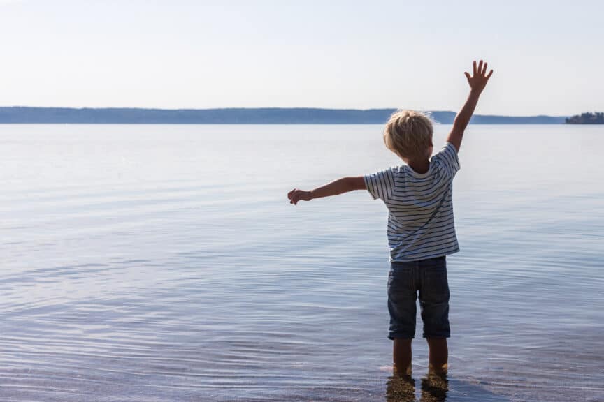 Boy standing in sea with arms raised