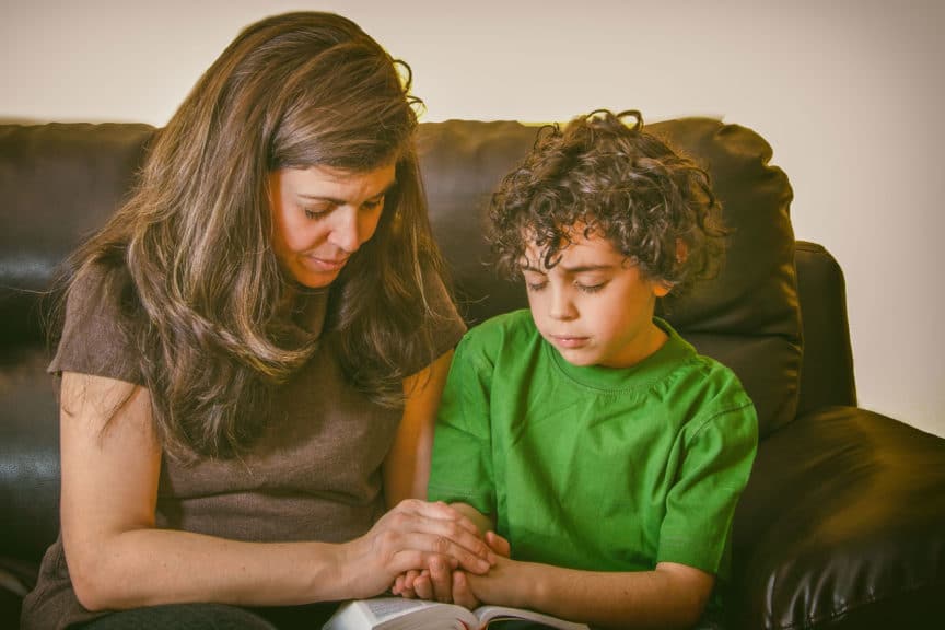 Close-Up Of Mother And Son Praying While Sitting On Sofa At Home