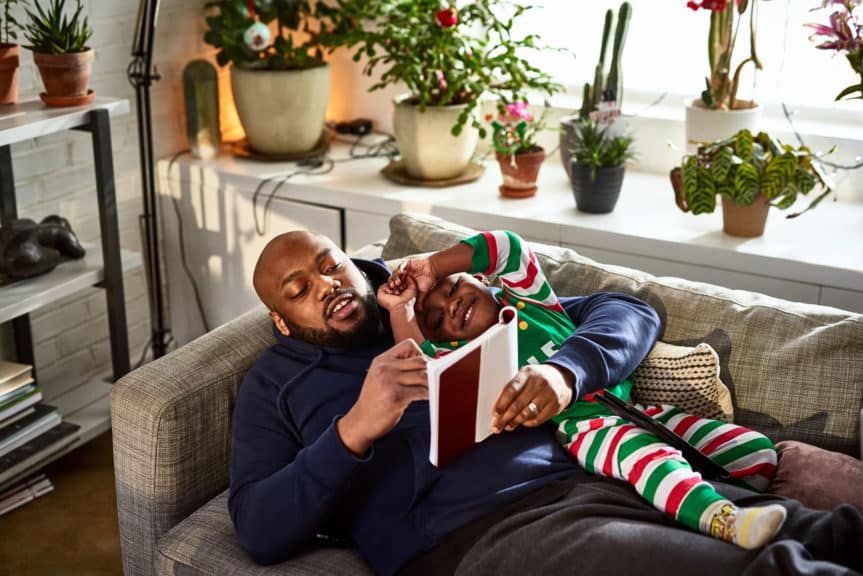 Father lying on sofa with son reading book