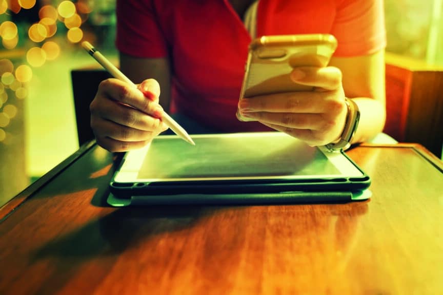 Closeup of someone using stylus pen on a tablet and phone in their hand