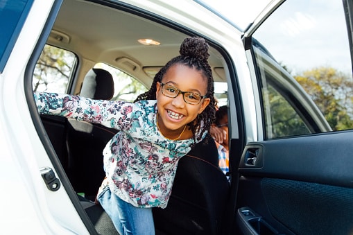 young african american girl standing and smiling out the back seat of a car