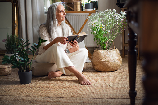 Relaxed senior woman sitting on floor and reading book