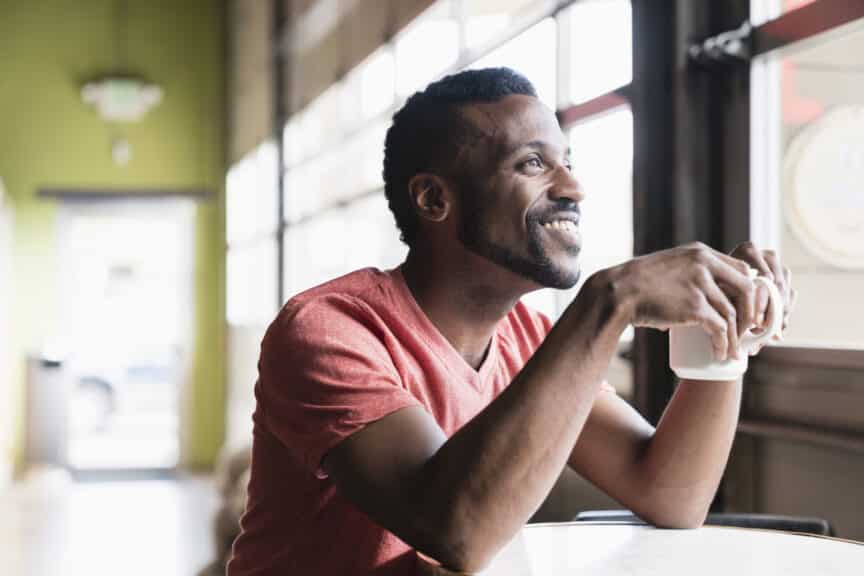 Smiling Black man sitting at window in coffee shop