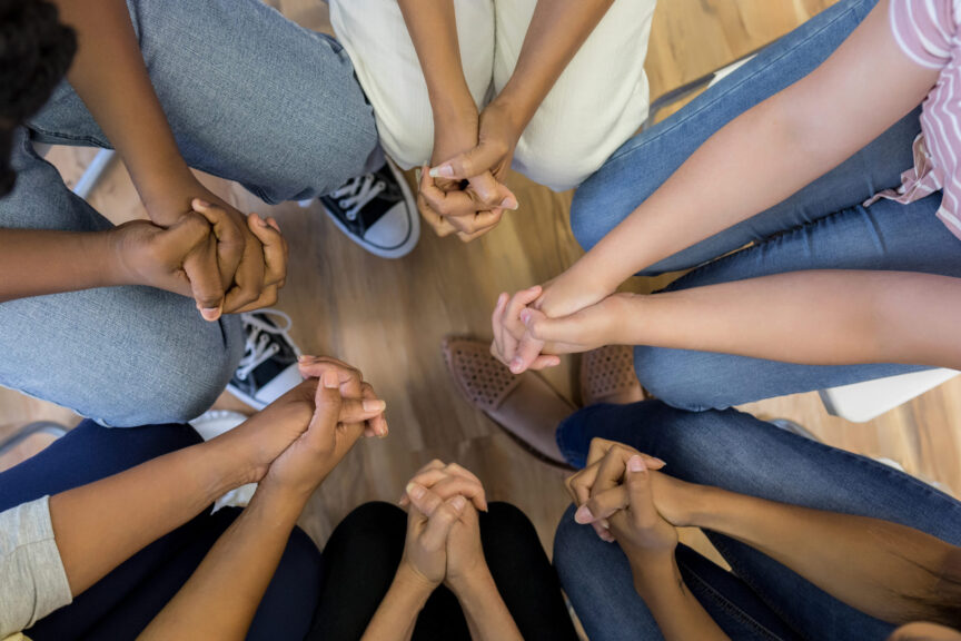 High angle view clasped hands of group sitting in circle
