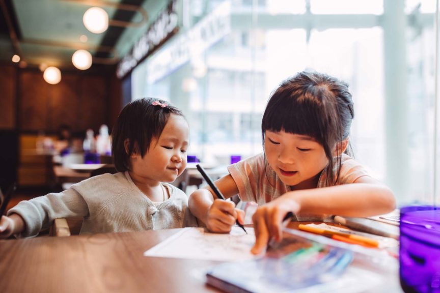 Little girl teaching her sister draw in a restaurant
