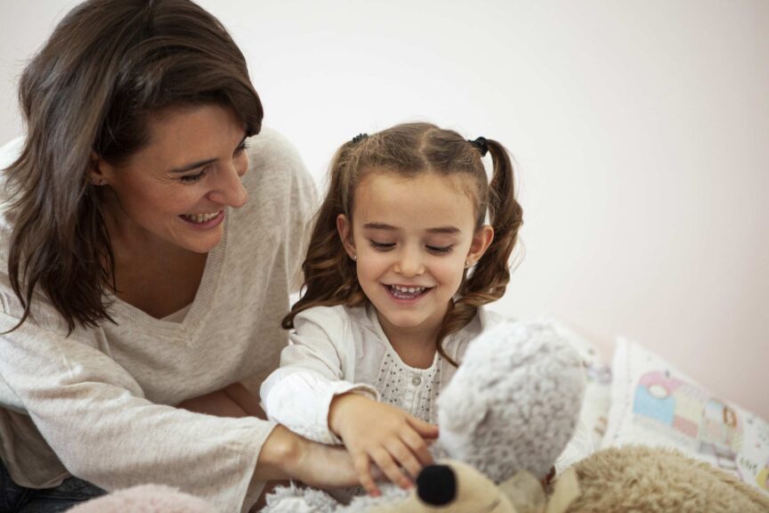 Mother and daughter playing with stuffed animals in bedroom