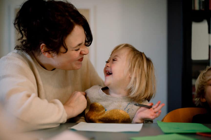 Mother-making-facial-expressions-while-playing-with-disabled-daughter-at-dining-table