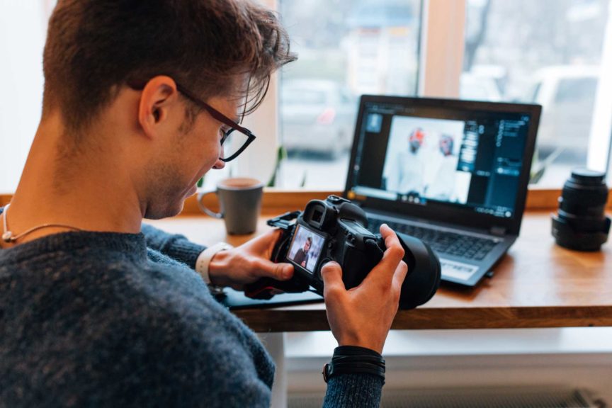 Photographer looks at photos in the professional camera at cafe with laptop