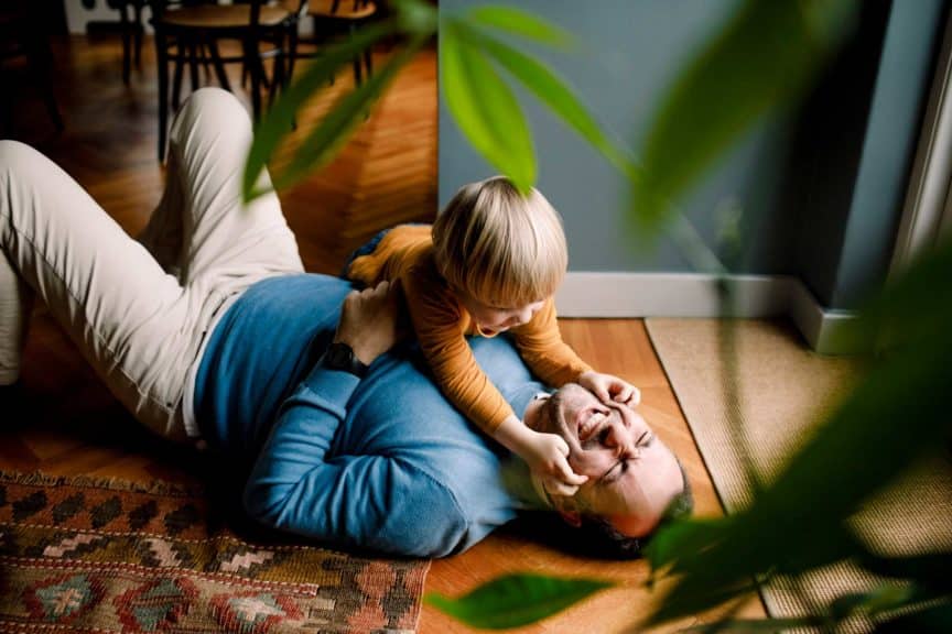 Playful daughter pinching cheerful father's cheeks on floor at home