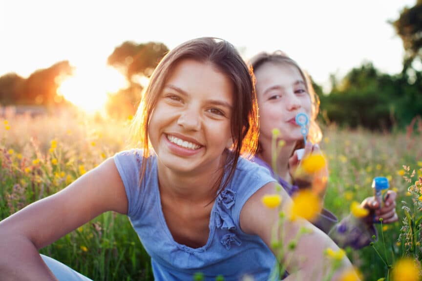 Portrait of girls sitting in field one blowing bubbles