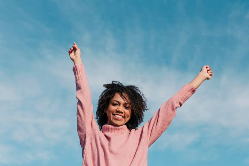 Portrait of smiling young woman against sky raising hands