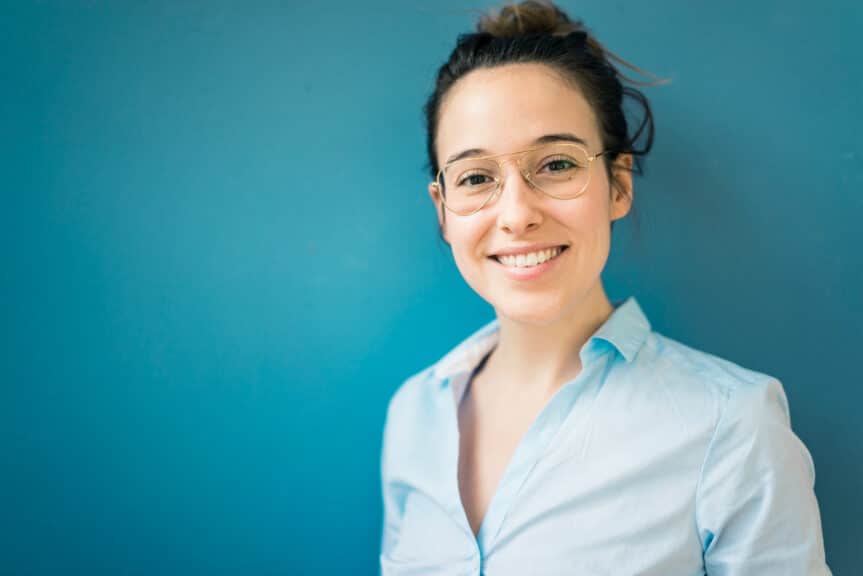 Portrait of smiling young woman wearing glasses in front of blue wall