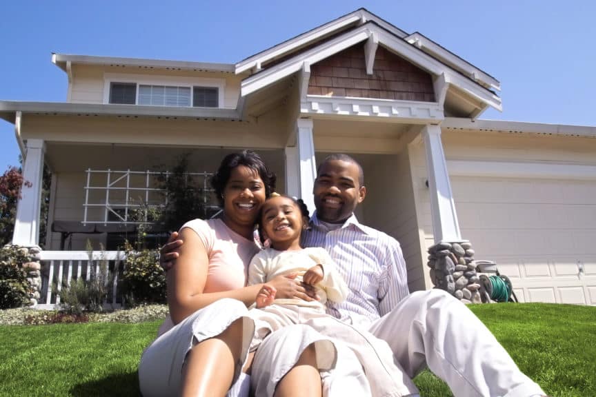 Portraif of a young family sitting on the lawn in front of their house.