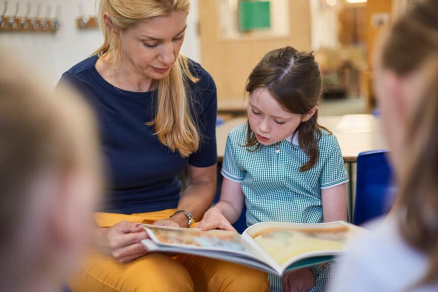 Teacher with schoolgirls reading storybook in classroom at primary school