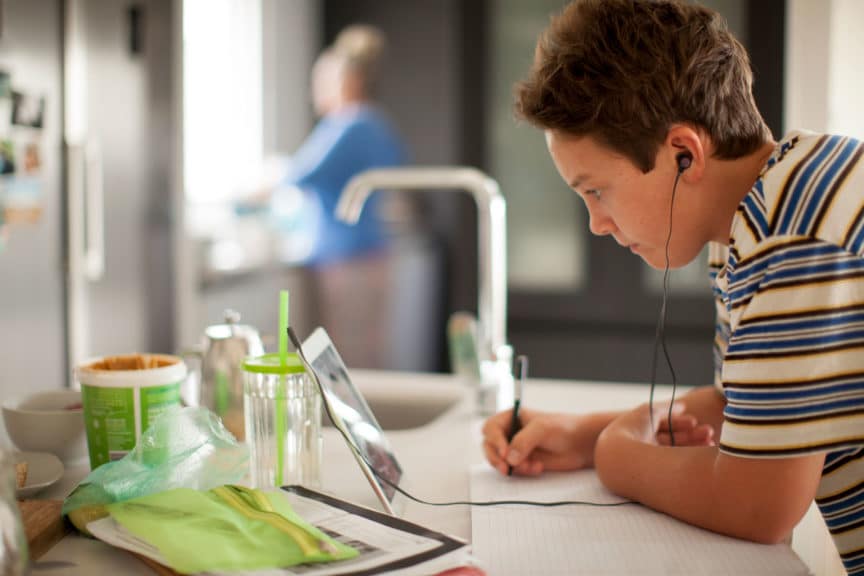 Young student working on digital tablet in his kitchen during lockdown