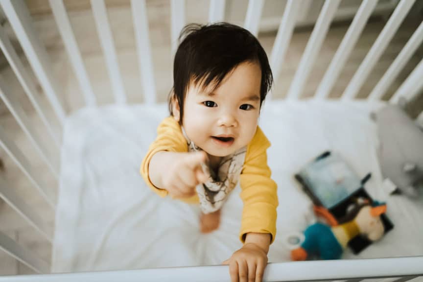 Adorable baby girl standing in her crib and pointing away with fingers