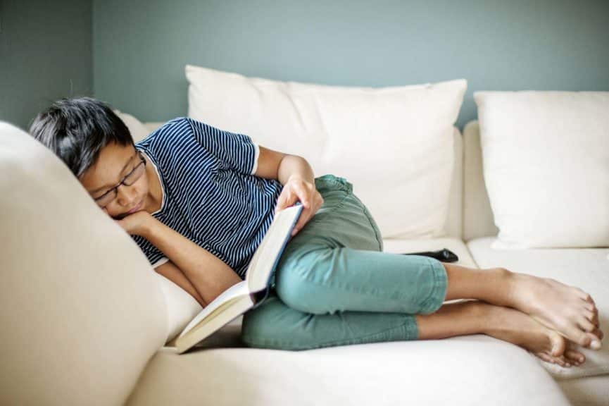 Boy reading book while lying on a sofa