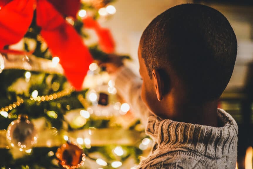 little boy standing at a Christmas tree with lights and decorations