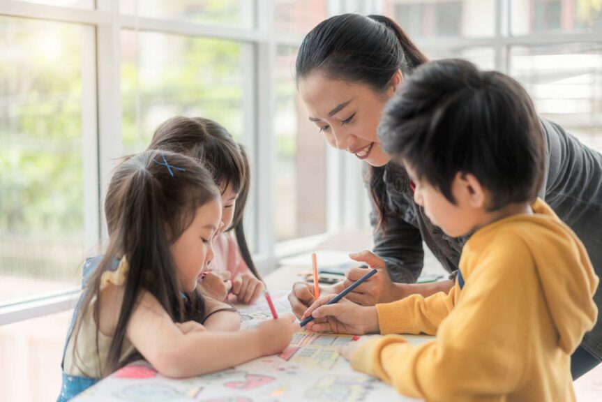 Children boys and girls sitting together around the table in classroom and drawing