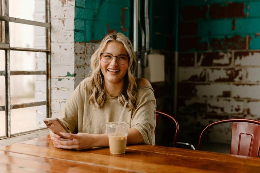 happy young adult woman smiling at table with phone in her hand