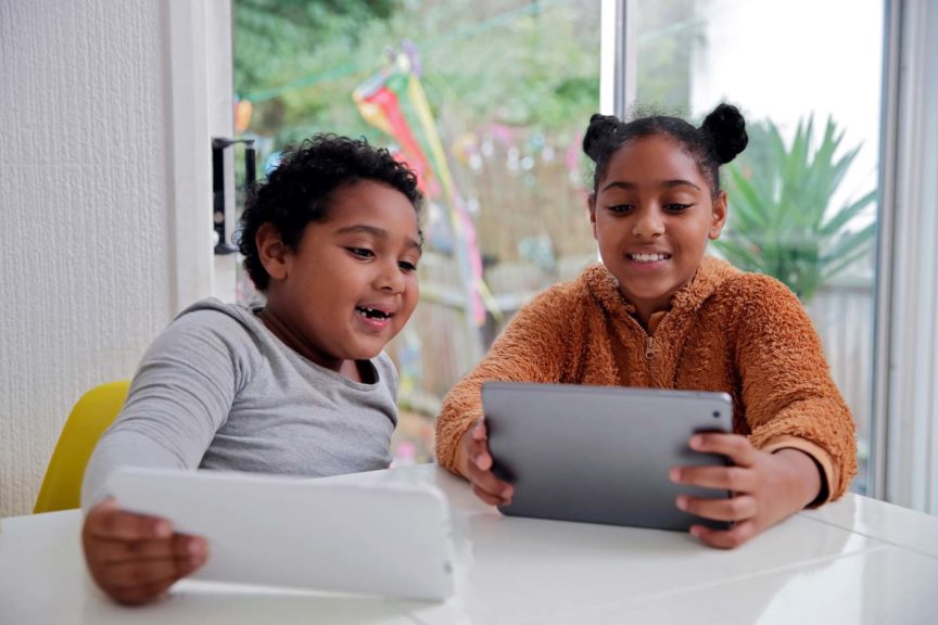 Brother and sister smiling and using digital devices