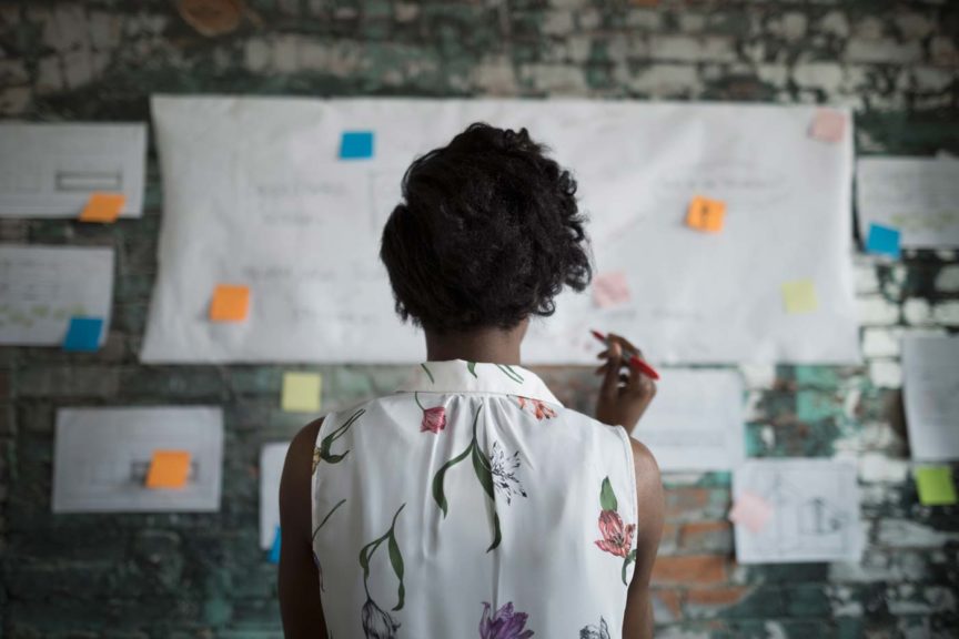 Creative businesswoman brainstorming, reviewing flow chart hanging on brick wall in office