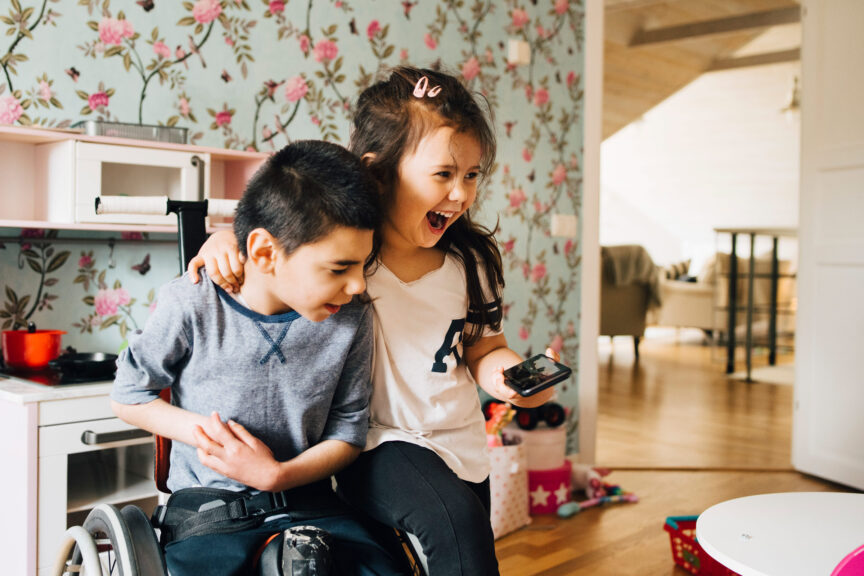 Cheerful sister watching video with autistic brother on smart phone at home