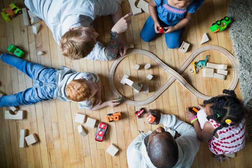 Overhead view fathers and children enjoying play date playing with toy train and wood blocks
