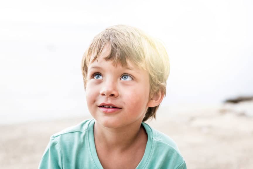 Close-Up Boy Looking Up While Sitting On Beach Against Sky