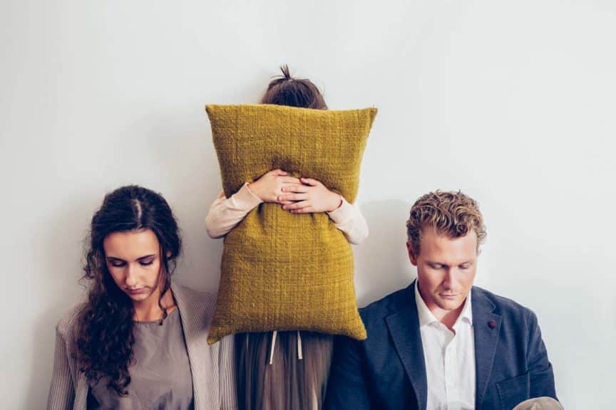 Couple having relationship conflict with their daughter hiding her face behind cushion