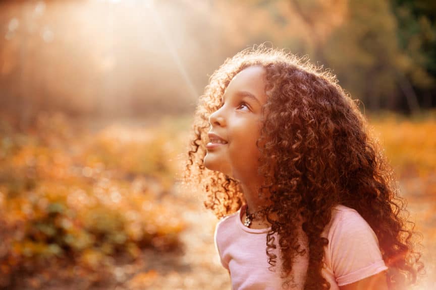 cute little girl with curly hair receives miracle sun rays from the sky