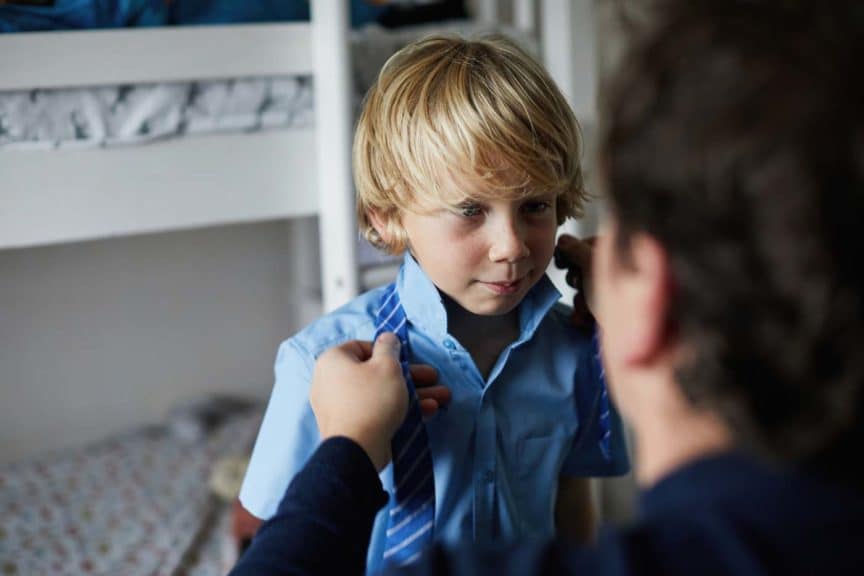 Father helping his son get ready for school by tying is school tie