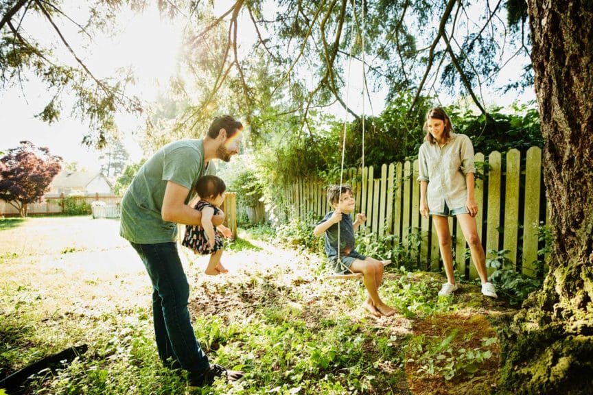 Family hanging out together at swing in backyard on summer morning