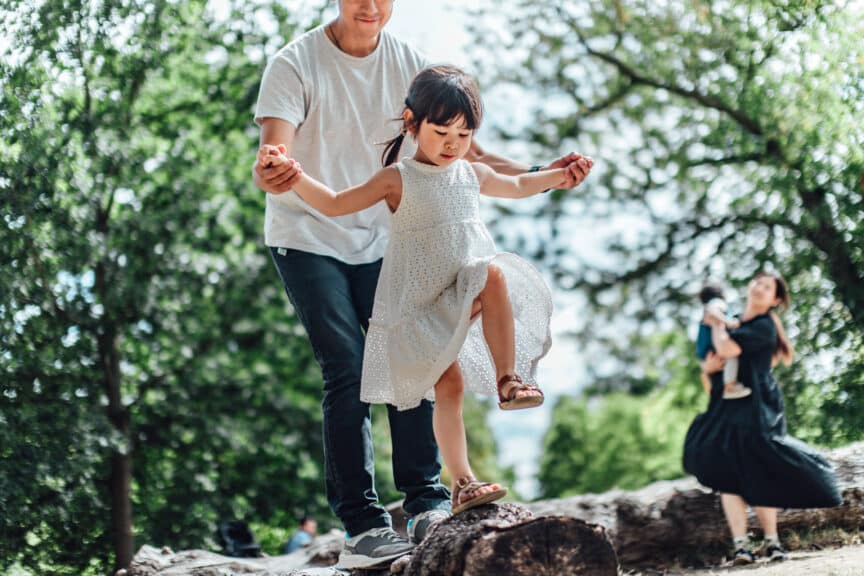 father holding hands of his little daughter and assisting her to walk along