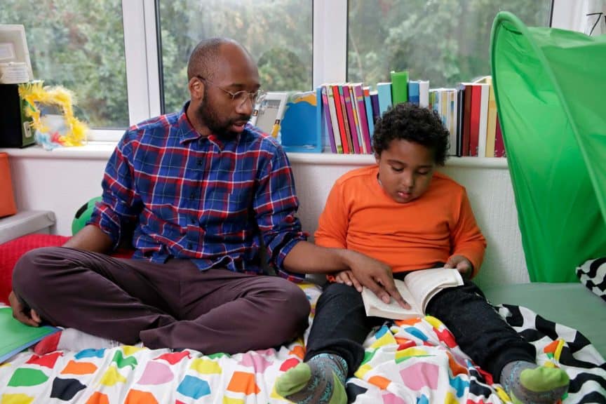 Father listening to son reading in bedroom