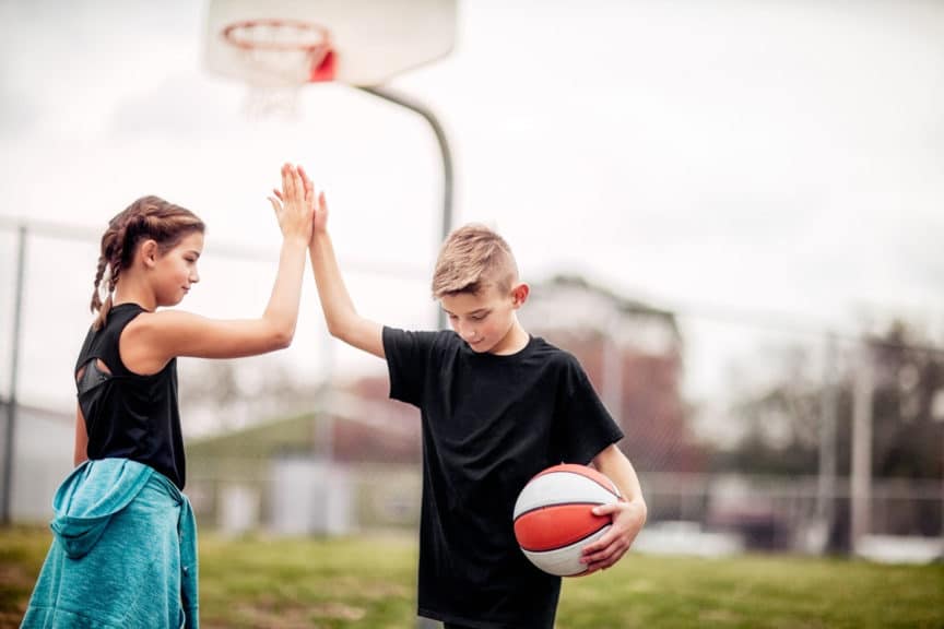 pre-teen boy and girl giving each other a high-five after basketball game