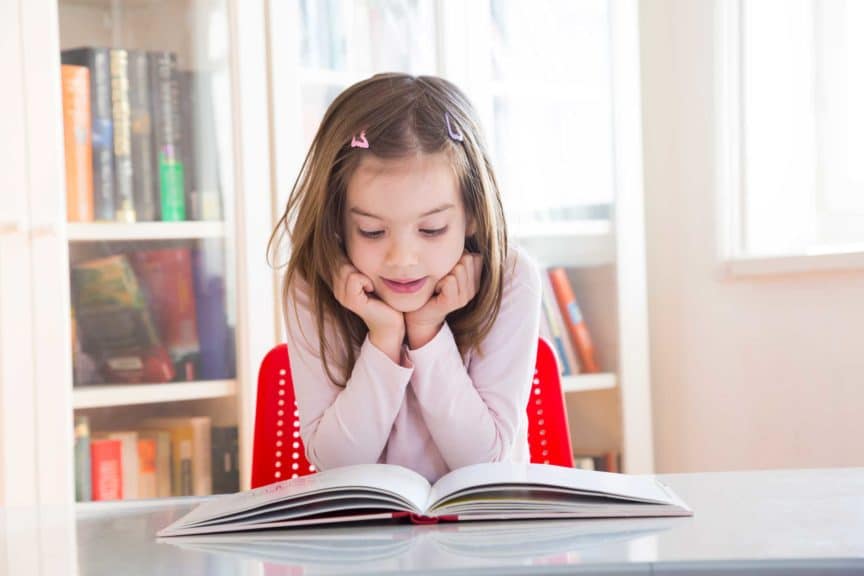 Portrait of little girl at table reading a book