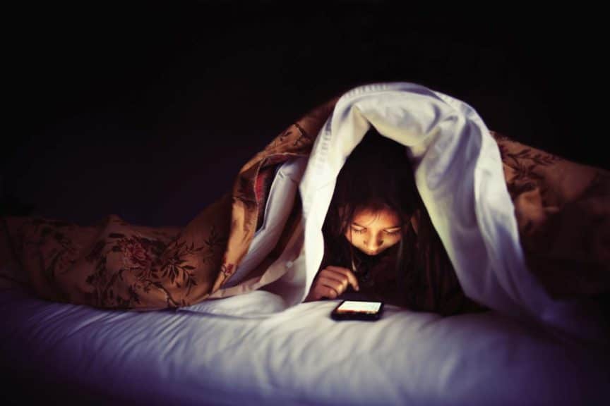 child reading look at smart phone under a blanket