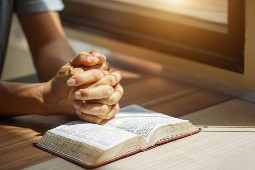 Hands of an unrecognizable a man with Bible praying 