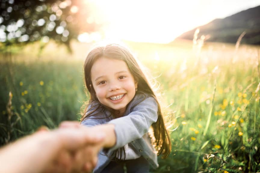 Happy small girl holding onto an adults hand outside in spring nature