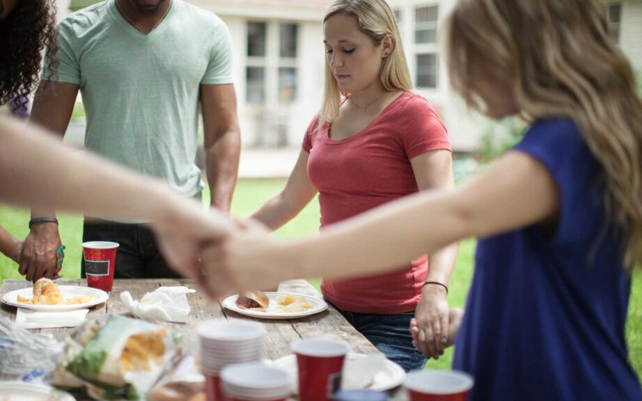 people holding hands and praying around a table.