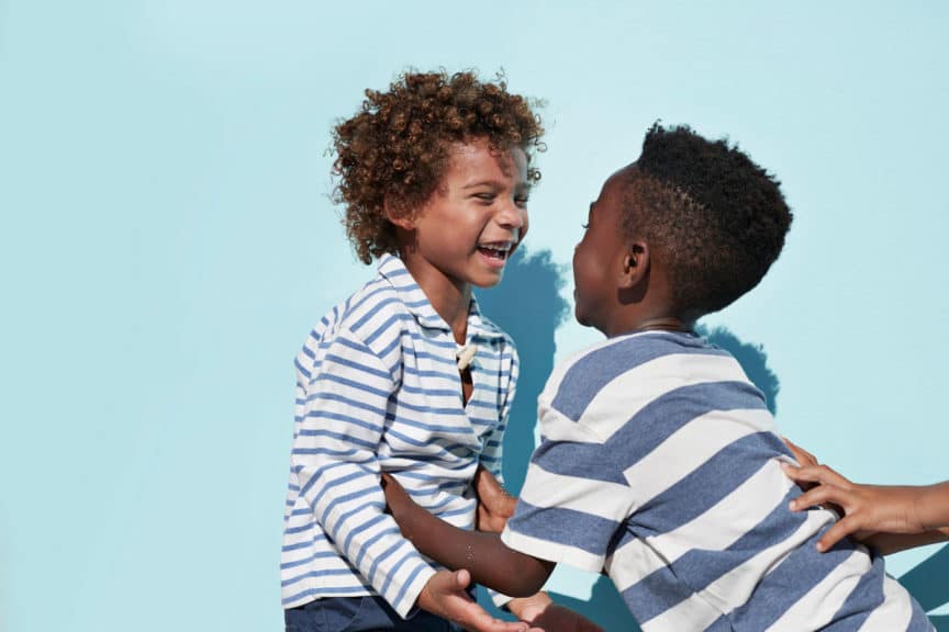 Portrait of kids hanging out & playing together on blue backdrop in sunlight