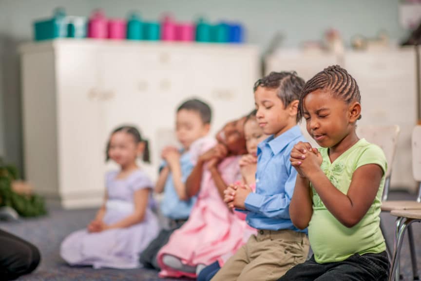 group of elementary age children are kneeling on the ground and are praying together