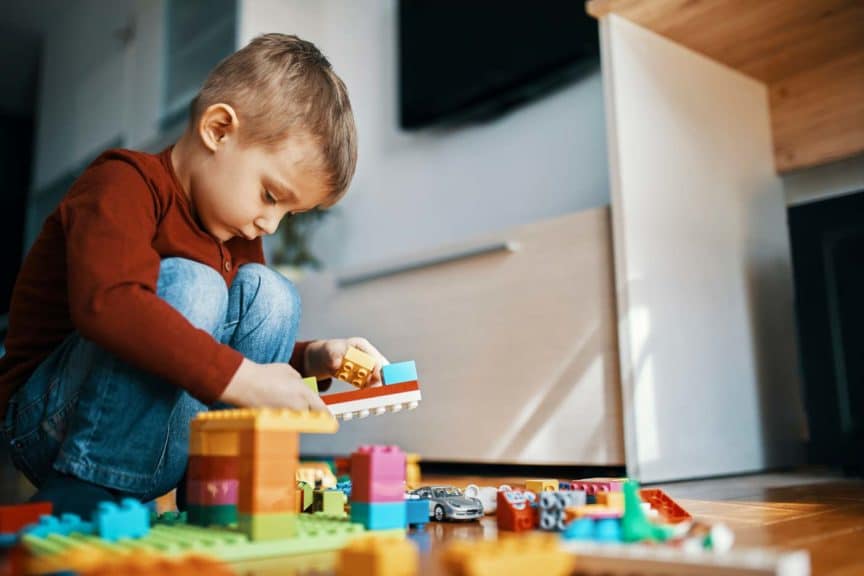 Little boy crouching on the floor at home playing with building bricks