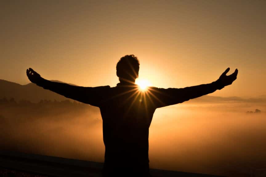 man with wide open arms in the mountains against the sun