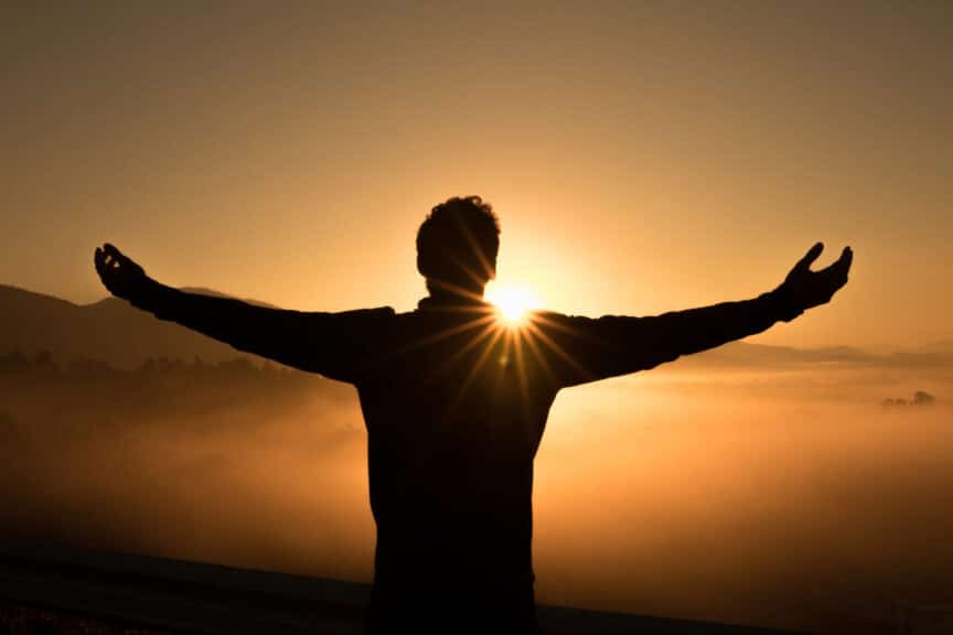 man-shadow-arms-wideopen-mountains-sun