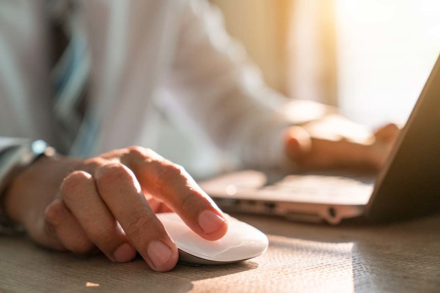 Hand holding computer mouse with laptop keyboard in the background